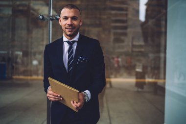 Klasör el kameraya gülümseyen Ise tutarak pahalı şık elbiseli başarılı olumlu işadamı portresi. Formal giyim daimi cam duvara neşeli Finans Müdürü