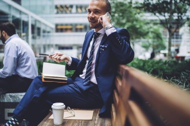 Pozitif girişimci kentsel için notlar not defteri ile belirleyen ve iş stratejisi tartışırken Smartphone'da konuşurken oturan şık elbiseli. Başarılı gurur ceo arama telefonu gezici