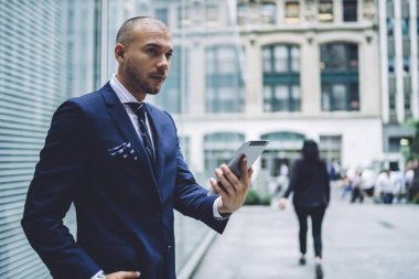 Kendine güvenen genç adam girişimci modern Dokunmatik ped cihaz tutan ve app ile online navigator yükleyip sokakta şehir merkezinde yürüyüş genel Internet kullanarak şık şık takım elbise giymiş