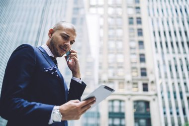 Smartphone üzerinde arama ve yüksek ofis gökdelenler ile şehir merkezinde genel Internet bağlantısı ayakta kullanarak modern dokunmatik yüzey üzerinde Web sitesinde online bilet rezervasyonu resmi aşınmaya başarılı iş adamı