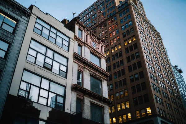 Exterior of modern constructed real estate with lights in office windows located in downtown, tall buildings with rental apartments for residents and commercial property for corporation and companie