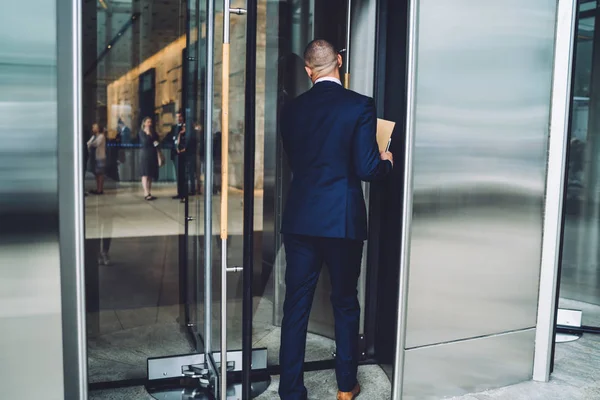 Back view of experienced businessman dressed in elegant suit come into office building via glass door.Male entrepreneur in formal wear going in financial company