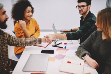 Yaratıcı çok kültürlü tasarımcılar ekibi toplantı masada oturan ortak proje geliştirme üzerinde işbirliği formal giyim giymiş. Genç erkekler el sıkışma işbirliğinin başarılı anlaşma sonra
