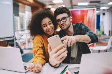 Pozitif Afro-Amerikan hippi kız ile birlikte neşeli beyaz genç adam modern smartphone ön kameraya gülümseyen ve selfie yayın için internet blog yapma rahat kıyafet giymiş