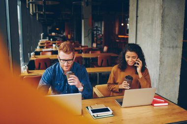 Genç kadın ve erkek meslektaşları, uzay, koyu tenli coworking kıza groupmate kitaplığı ile ödev yaparken cep arama yakın oturan dizüstü bilgisayarlar üzerindeki çalışmalarını tamamladıktan