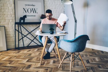 Kağıt belgeleri posta modern dizüstü bilgisayarda kablosuz internet bağlantısı kullanarak kontrol elinde olan dalgın genç adam. Grafik tasarımcı netbook şık daire içinde serbest çalışma