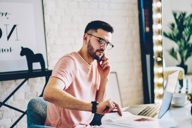 İşleç için smartphone: çağrı ve modern dizüstü dairede oturan banka hesabınızı kontrol genç adam. Hipster adam serbest meslek sahibi cep üzerinde çalışma işlemi sırasında netbook evde konuşmak.