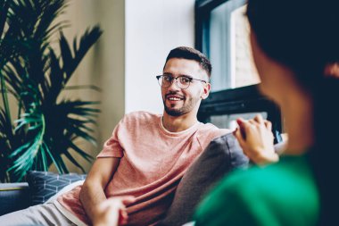 Neşeli yakışıklı genç kız elele ve boş vakit konfor apartman dairesinde Eyewear. Pozitif kocası evde karısı ile birlikte rahat kanepede rahatlatıcı