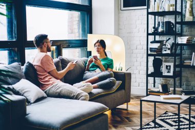 Çift rahat koltukta istirahat ve süre bloglama üstünde smartphones modern daire ev Internet bağlantısı kullanarak birbirleriyle iletişim kurmak aşık. Genç evlilik evde kanepede rahatlatıcı