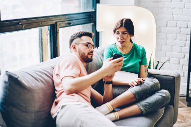 İnternet Yayıncılığı modern smartphone cep telefonu ile internet sitesinde kız arkadaşına ortak şık daire içinde rahat kanepede rahatlatıcı gösterilen genç adam. Koca karısıyla tarassut video blog cep