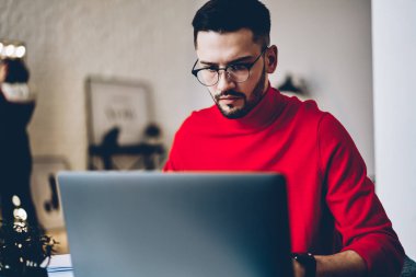 Genç adam için vizyon düzeltme izlerken özel öğretmen evde kablosuz Internet bağlantısı kullanarak dizüstü bilgisayarda internet sitesinde gözlük içinde yoğunlaşmıştır. Dalgın hipster adam netbook, serbest çalışma