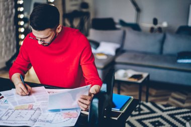 Genç adam notlar metin bilgi vasıl okul sırası modern apartmanda oturan kağıt belgeler üzerinde yoğunlaşmıştır. Casual dalgın hipster öğrenci ödev hazırlama semineri için aşağı yazma giyinmiş