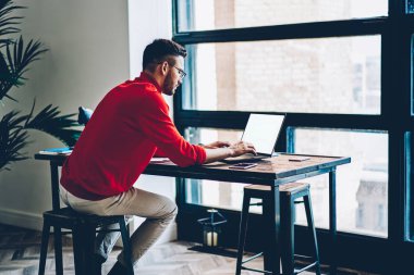 Dizüstü bilgisayar aygıt vasıl okul sırası oturan kablosuz bağlantı kullanarak internet sitelerinde bilgi arama dalgın genç adam. Akıllı hipster öğrenci bilgi ders çalışma için netbook klavye