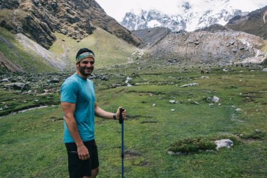 Yeşil manzara ve arka plan üzerinde yüksek Dağları'nın muhteşem sahne kamera ayakta yolculuk tutkusu hafta sonu hiking sırasında gülümseyen aktif giyim mutlu erkek traveler portresi giymiş
