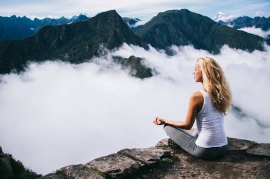 Lotus kayalık tepenin zevk kenarında oturup meditasyon yaparken sarı saçlı sarışın genç kadın zaman yolculuğunun sakin ol. Kadın turist sakin doğanın tadını yüksek tepe dağdan yoga yaparken