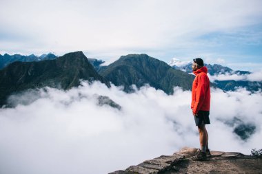 Sakin ve ilham yüksek yeşil dağların tadını aktif giyim giyinmiş deneyimli erkek Turizm Zirvesi kenarında duran beyaz sis kaplı. Nefes kesen manzaranın genç adam traveler