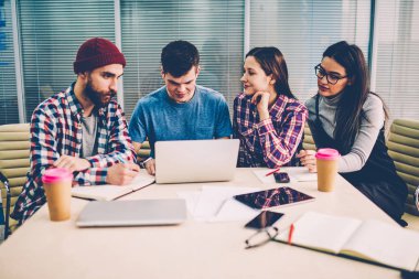 Genç yetenekli hipster adam yanında oturan ve eğitim için yeni app kampüs içinde öğrenciler ortak proje araştırma bağlantılı yapma hakkında konuşmak yüklemek yardımcı meslektaşları süre dizüstü bilgisayar kullanan