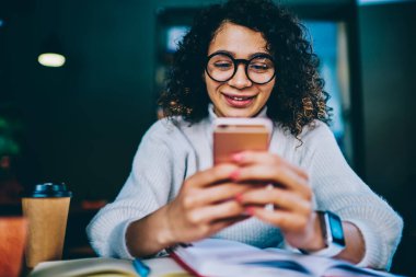 Kadın blogger göstermek tatilinde trendy gözlük cep üzerinden arkadaşımdan olumlu e-posta okuma mutlu kadın Kullanıcı kafede oturan okuyan smartphone online komedi izlerken gülümsüyor