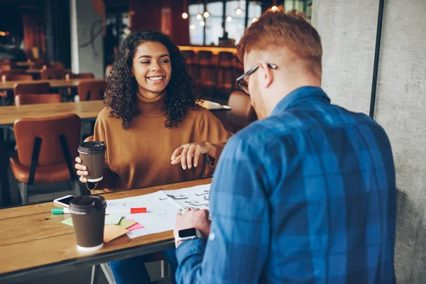 Smiling african american girl having fun during meeting with back view friend on break , cheerful young woman share successful ideas  and good news with male colleague talking with coffee in cafe