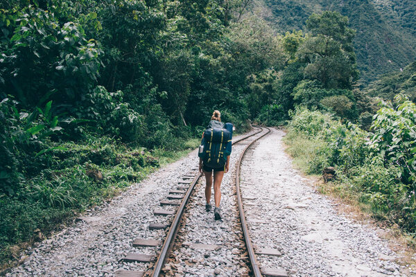 Back view of experienced young woman traveler with tourist backpack going on railway exploring green vegetation during hiking wanderlust in mountains.Female hiker in active wear discover new places