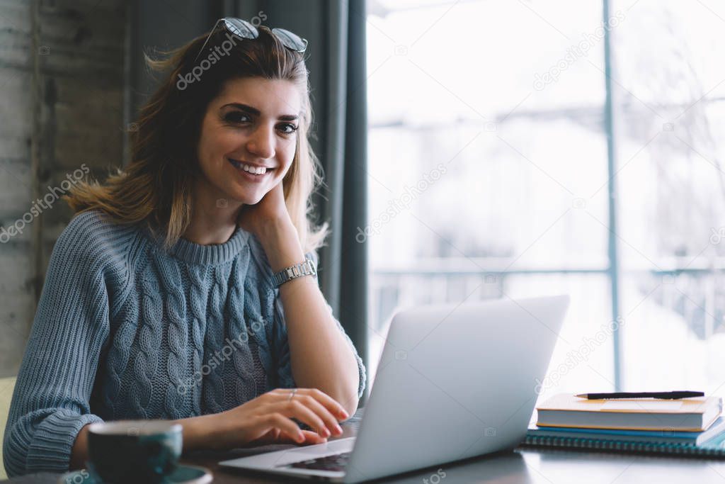 Portrait of successful millennial female software developer looking at camera in break of work on laptop computer, smiling it professional enjoying distance job waiting webinar sitting at cafeteria