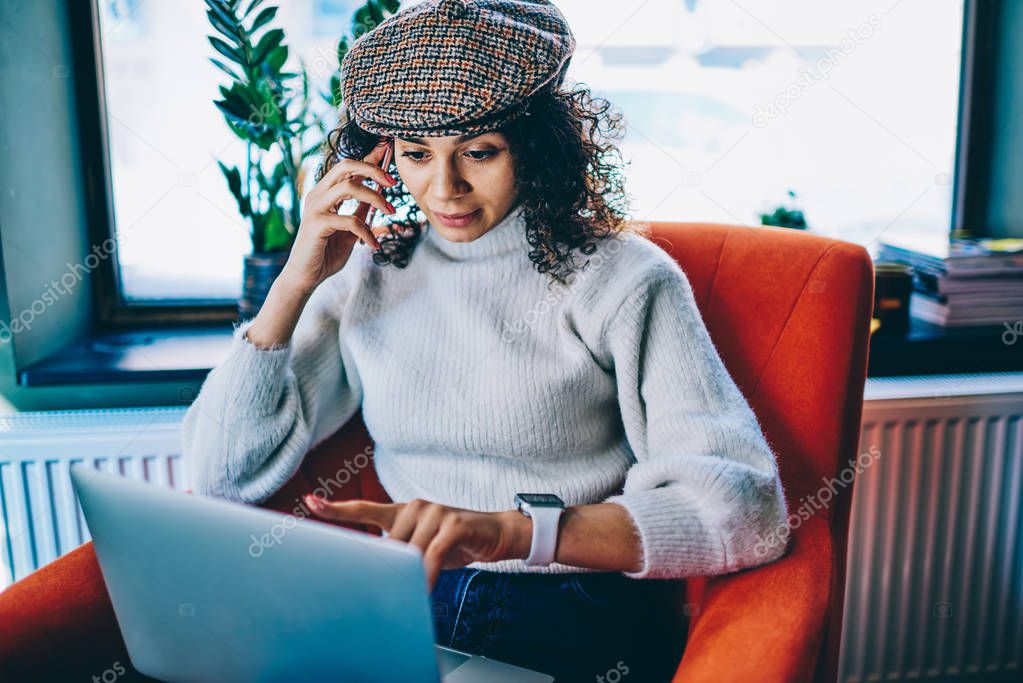 Young concentrated female programmer making serious telephone conversation with employer looking mistakes on website, trendy hipster girl calling to customer service consulting about repairing netbook