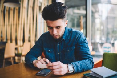 Genç adam iç Web sitesi holding kredi kartından rezervasyon ve smartphone, ciddi hipster adam para denge yolu ile hücresel kullanma kafede oturan denetimi kullanmak için ödeme yapmadan konsantre