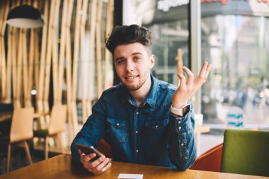Kamera Cafe iç modern smartphone tutan bakarak karışık genç adam portresi, sorguya yakışıklı duygusal hipster adam gelir metin iletisi telefonla bildirim alma hakkında