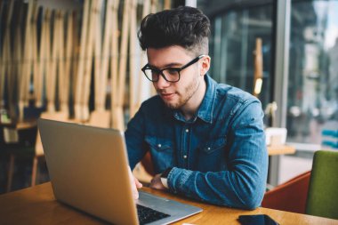 Yetenekli erkek programcı aşınma gözlükler gözleri koruma serbest dizüstü bilgisayar üzerinden üzerinde çalışırken, akıllı öğrenci netbook eğitsel izlerken kafeterya derslerde öğrenme e memnun.