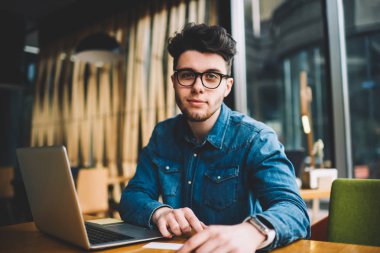 Yetenekli erkek portresi bu kafe iç kablosuz bağlantı ve dizüstü bilgisayar, gözlük vizyon koruma netbook ile öğrenme süre için genç adam kullanarak uzaktan çalışan geliştirici