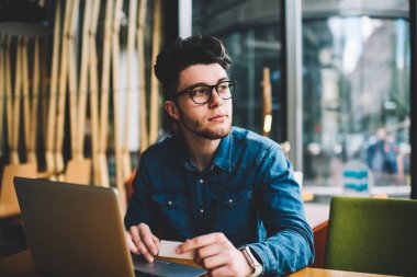 Uzak netbook ve ziyaret kartı ile dizüstü bilgisayarda uygulama bankacılık yolu ile onun kredi kartından transfer para yapma hakkında düşünme dalgın adam masada oturan gözlük arıyorum Genç hippi herif