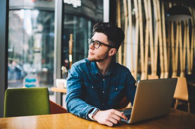 Yakışıklı delikanlı Eyewear kafe iç, hipster adam uzakta istimal Wi-Fi bağlantısı ve netbook kafeteryada uzaktan çalışırken seyir içinde dizüstü bilgisayar ile masada oturan arkadaş bekliyor