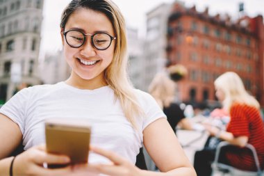 Gözlük rekreasyon açık havada modern cihaz ile zevk çekici başarılı kadın blogger kırpılmış görüntü. Komik Haberler okuma ve içtenlikle Sokağı'nda gülüyor sevimli duygusal kadın kapatmak