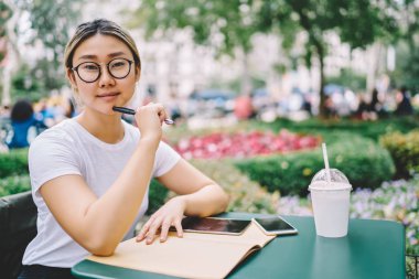 Yarım uzunluk portre sevimli yaratıcı Asyalı kadın Blogger şık beyaz t-shirt hakkında yaratıcı fikirler durulması içinde giyinmiş. Sevimli kadın kentsel ayarı, program planlama yaparken kameraya arıyor
