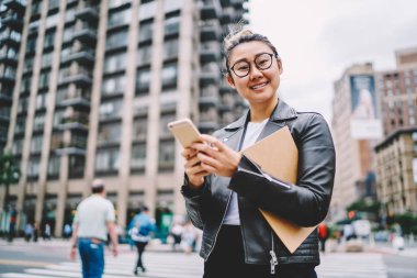 Modaya uygun kıyafeti giymiş genç başarılı kadın Blogger yarım uzunluk portre rekreasyon Sokağı'nda yürüyüş tadını çıkarın. Modern teknoloji kentsel ayarda gezinme sırasında kullanarak çekici pozitif kadın