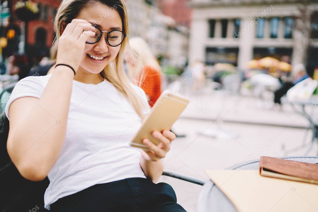 Cropped image of pretty emotional asian female person in eyeglasses for better vision watching funny video in website.Cute cheerful hipster girl sending messages to friends via application on phone