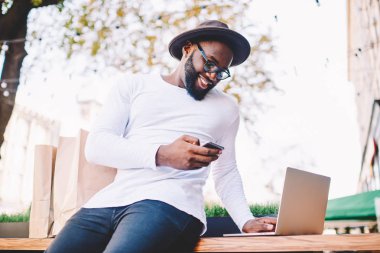 Afro-Amerikan blogger satış yapma dizüstü bilgisayar ve cep telefonu alışveriş online zevk gülümseyen adam web mağaza alımları indirimler, mutlu satın şık giysiler içinde neşeli koyu derili