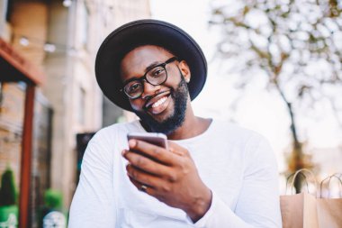 Memnun koyu tenli erkek alıcı yolu ile smartphone ve 4 g internet açık, neşeli Afro-Amerikan hipster adam cep kullanarak web mağazada alışveriş zevk çevrimiçi alışveriş yapma portresi