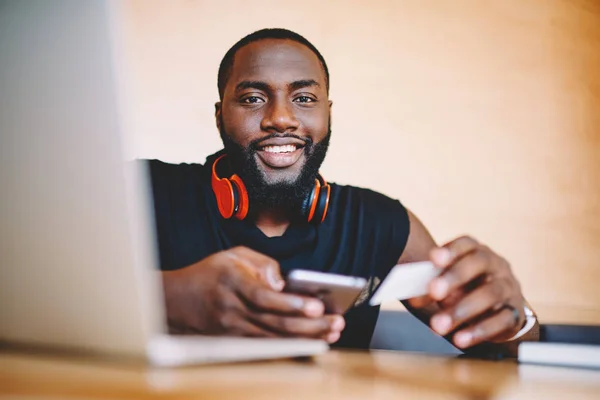 Portrait of cheerful dark skinned man using banking app on mobile phone for checking balance on card, smiling african american man satisfied with successful money transaction via smartphone