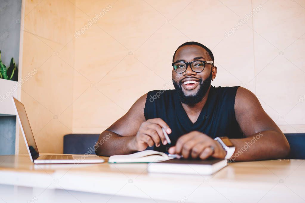 Portrait of cheerful african american guy learning in library using laptop computer satisfied with online course, smiling dark skinned man freelancer looking at camera during remote job in office