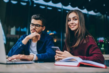 Cep telefonu kullanarak kameraya bakan genç kadın, netbook'ta görme koruması için gözlüklü erkek arkadaşı, kafe terasında teknoloji ve wifi kullanmayı öğrenen genç gençler