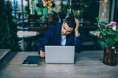 Kafe iç dizüstü bilgisayar ile oturan Pensive hipster adam bluetooth bağlantısı üzerinden multimedya paylaşmak, netbook ve kablosuz internet kullanarak serbest çalışan kafkas bin yıllık adam