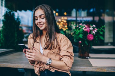Pozitif güzel esmer kız arkadaşı ile online sohbet akıllı telefon üzerinden metin mesajı gönderme, cep telefonu ve wifi bağlantısı kullanarak gülümseyen büyüleyici genç kadın boş zamanlarında kafede oturan