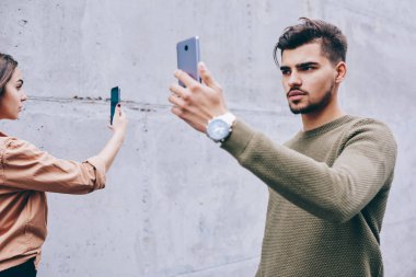 Ciddi erkek blogger sokakta açık havada gezinirken canlı video takipçileri ile sohbet, genç bin yıllık kadın ve erkek modern cihazlar ve cep telefonu kullanarak online iletişim bağımlılığı olan