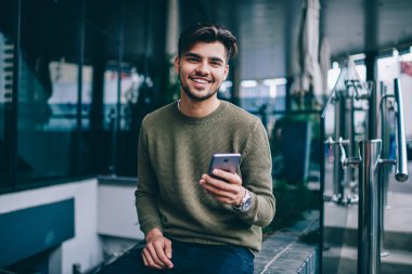 Sohbet ve ağ için cep telefonu ve kablosuz internet kullanarak neşeli yakışıklı erkek Portresi , mesaj göndermek için iyi 4g bağlantısı ile memnun kamera bakarak genç hipster adam