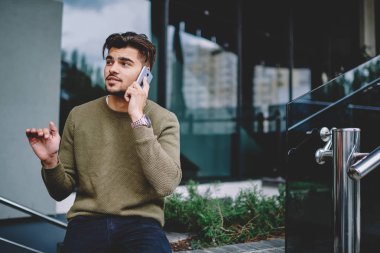 Yakışıklı adam açık havada oturan telefon görüşmesi sırasında bilgi açıklayan, hipster adam cep telefonu ile servis operatörü ile konuşma rezervasyon yapma danışmanlık detayları tartışıyor