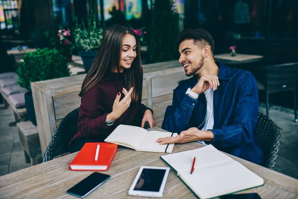 元気な女性と男性がノートと一緒にカフェテラスに座って計画を立て メモ帳からの情報を伝える笑顔のヒップスターが一緒に研究を楽しむ — ストック写真