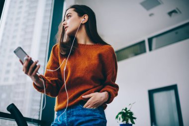 Cep telefonu, kulaklık düşünceli kadın uzağa bakarak uygulama üzerinden favori müzik çalma listesi dinlerken romantik şarkı kelimeler üzerinde düşünme düşünceli kadın meloman duygu