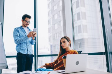 İş ve iş için teknoloji kullandıktan sonra fikir üzerinde kafa bilgisayara masaüstünde oturan Kafkas kadın iş arkadaşları ile online sohbet için akıllı telefon gadget ile yakın duran erkek ortağı ile işbirliği
