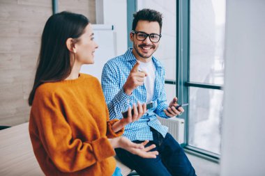 Akıllı telefon araçları üzerinden bilgi paylaşımı için kadın meslektaşı ile işten mola sırasında kameraya gülümserken optik gözlük işaret neşeli bin yıllık hipster adam Portresi